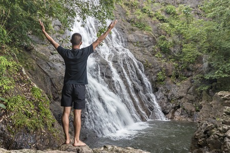 Back view of the man wear in relax outside on the rock and looking at the waterfall view.の写真素材