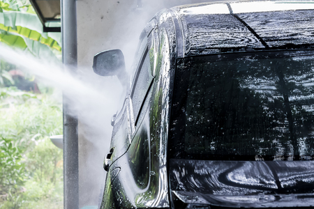 A man car wash with black car, washing with foam and water pressure at carwash.の写真素材