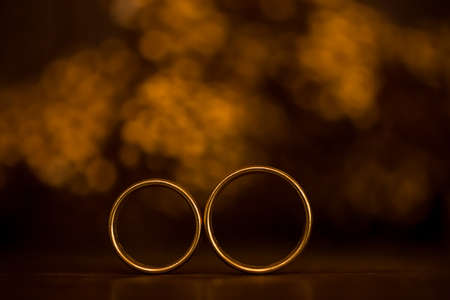 Wedding gold rings standing in front of gold brown bokehの写真素材