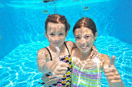 Happy active kids swim in pool and play underwater, girls diving and having fun, children on summer  vacation, sport conceptの写真素材