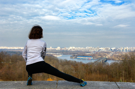 Woman runner stretching with beautiful city view, jogging and working out outdoorsの写真素材
