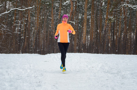 Winter running in forest: happy woman runner jogging in snow, outdoor sport and fitness conceptの写真素材