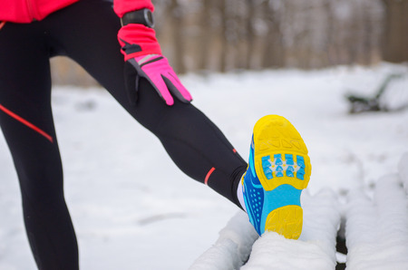 Winter running in park: sportswear closeup in snow, woman stretching before jog, outdoor fitness and...