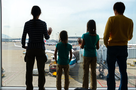 Family in airport, travel concept, silhouettes of parents with kids in terminal waiting for flight and looking at airplanesの写真素材