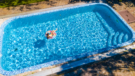 Aerial view of girl in swimming pool from above, kid swim on inflatable ring donut and has fun in...