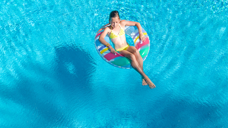 Aerial view of girl in swimming pool from above, kid swim on inflatable ring donut and has fun in...