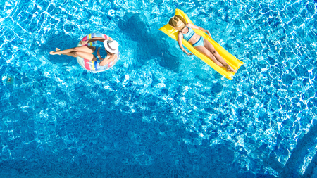 Aerial drone view of children in swimming pool from above, happy kids swim on inflatable ring donuts, girls have fun in water on family vacationの写真素材