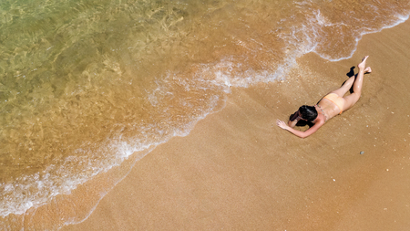 Aerial top view of young woman in bikini relaxing on sand tropical beach by sea and waves from above, girl on tropical island beach vacation in Thailandの写真素材