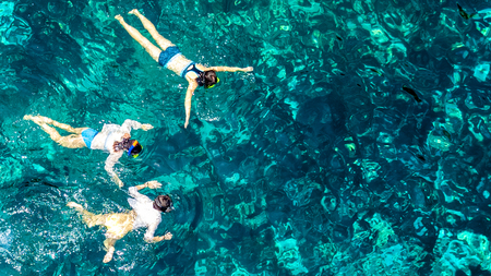 Aerial top view of family snorkeling from above, mother and kids snorkelers swimming in a clear tropical sea water with corals during summer vacation in Thailandの写真素材
