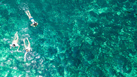 Aerial top view of family snorkeling from above, mother and kids snorkelers swimming in a clear tropical sea water with corals during summer vacation in Thailandの写真素材