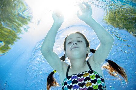 Child swims underwater in swimming pool, happy active teenager girl dives and has fun under water, kid fitness and sport on family vacation on resortの写真素材