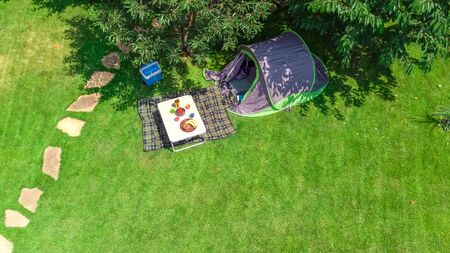 Aerial top view of campsite from above, tent and camping equipment under tree, family vacation in...