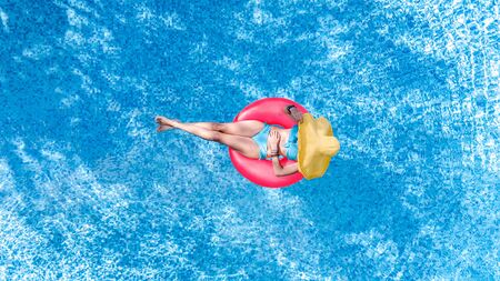Beautiful young woman in hat in swimming pool aerial top view from above, young girl in bikini relaxes and swims on inflatable ring donut and has fun in water on family vacation, tropical holiday resortの写真素材
