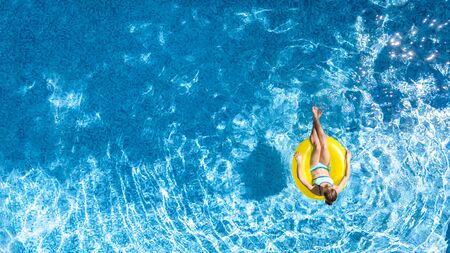 Active young girl in swimming pool aerial top view from above, child relaxes and swims on inflatable ring donut and has fun in water on family vacation, tropical holiday resortの写真素材