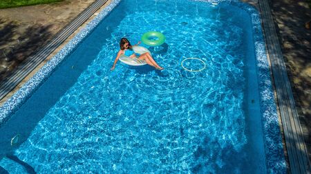Aerial view of beautiful girl in swimming pool from above, swim on inflatable ring donut and has fun...