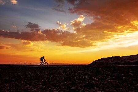 Silhouette of cycling man on bike on beautiful sunset backgroundの写真素材