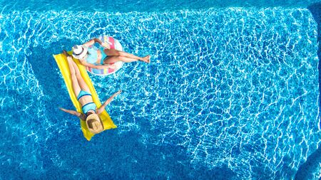 Children in swimming pool aerial drone view fom above, happy kids swim on inflatable ring donut and mattress, active girls have fun in water on family vacation on holiday resortの写真素材