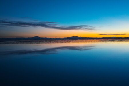 Sunrise on Salar de Uyuni in Bolivia covered with water, salt flat desert and sky reflectionsの写真素材