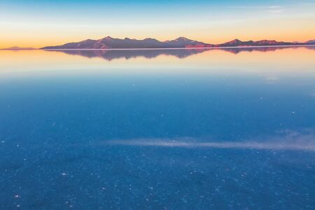 Sunrise on Salar de Uyuni in Bolivia covered with water, salt flat desert and sky reflectionsの写真素材