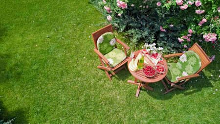 Decorated table with bread, strawberry and fruits in beautiful summer rose garden, aerial top view of romantic date table food setting for two from aboveの写真素材
