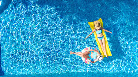 Children in swimming pool aerial drone view fom above, happy kids swim on inflatable ring donut and mattress, active girls have fun in water on family vacation on holiday resortの写真素材