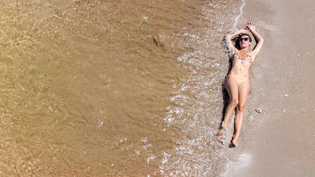 Aerial top view of young woman in bikini relaxing on sand tropical beach by sea and waves from...