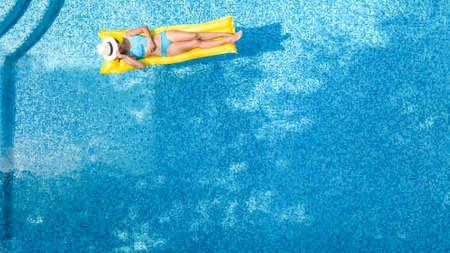 Beautiful young girl relaxing in swimming pool, swims on inflatable mattress and has fun in water on family vacation, tropical holiday resort, aerial drone view from aboveの写真素材