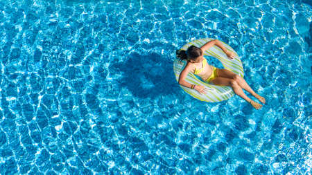Aerial drone view of little girl in swimming pool from above, kid swims on inflatable ring donut , child has fun in blue water on family vacation resortの写真素材