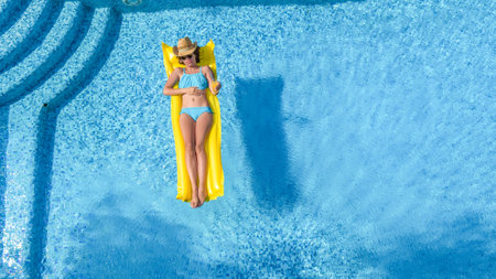 Beautiful young girl relaxing in swimming pool, woman swims on inflatable mattress and has fun in...