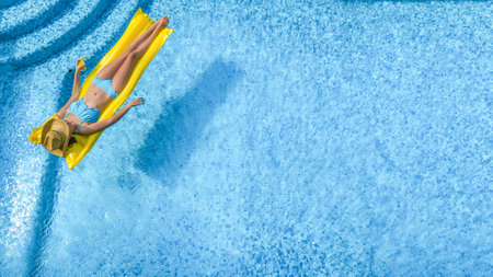 Beautiful young girl relaxing in swimming pool, woman swims on inflatable mattress and has fun in...