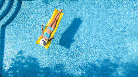 Beautiful woman in hat in swimming pool aerial top view from above, young girl in bikini relaxes and swims on inflatable ring donut and has fun in water on family vacation, tropical holiday resortの写真素材