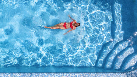 Active young girl in swimming pool aerial drone view from above, young woman swims in blue water...