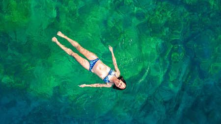 Young woman swimming in blue sea lagoon in crystal clear water, girl in bikini swims and relax, aerial drone view from aboveの写真素材