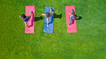Family fitness and sport outdoors, group of active girls doing workout in park, active women exercising outdoor on green grass, aerial top view from aboveの写真素材