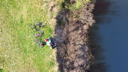 Family on bikes cycling outdoors, active parents and kids on bicycles, aerial view of family with children relaxing near beautiful river from above, sport and fitness conceptの写真素材