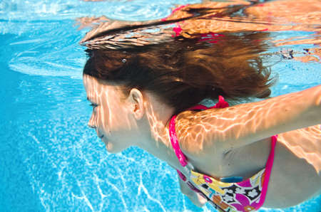 Child swims underwater in swimming pool, active little girl dives and has fun under water, kid fitness and sport on family vacationの写真素材