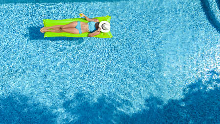 Beautiful woman in hat in swimming pool aerial top view from above, young girl in bikini relaxes and...