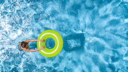 Active young girl in swimming pool aerial top view from above, teenager relaxes and swims on inflatable ring donut and has fun in water on family vacation, tropical holiday resortの写真素材