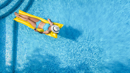 Beautiful woman in hat in swimming pool aerial drone view from above, young girl in bikini relaxes...