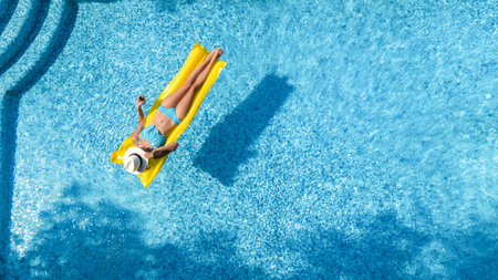 Beautiful woman in hat in swimming pool aerial drone view from above, young girl in bikini relaxes...