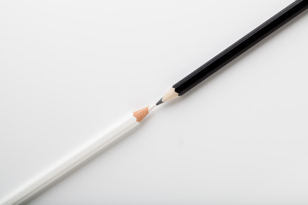 White pencil and black pencil pointing each other