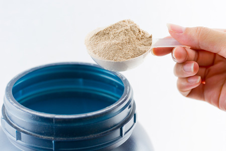 The hand raise a spoon measure Whey protein chocolate powder for fitness and bodybuilding gaining muscle.の写真素材