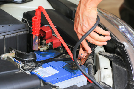 Car mechanic uses battery jumper cables charge a dead battery.