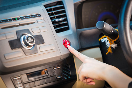 Female hand pressing emergency light button on car dashboard.の写真素材