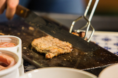 Hand cutting a slice of pork meat on chopping wood.の写真素材
