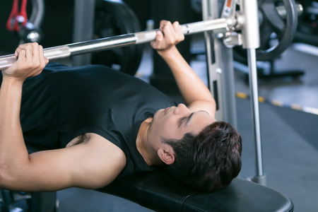 Man lifting dumbbell weights while lying down in gym.の写真素材