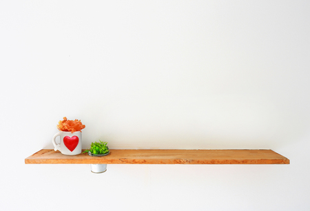 Wooden shelf on white wall with green plant and mug heart.の写真素材