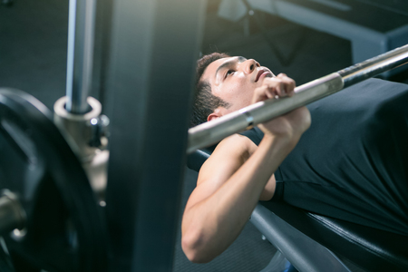Man lifting dumbbell weights while lying down in gym.の写真素材