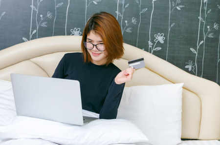 Happy woman doing online shopping at home on bed.の写真素材
