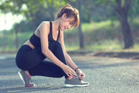 Closeup of woman tying shoe laces. Female sport fitness runner getting ready for jogging outdoors.の写真素材